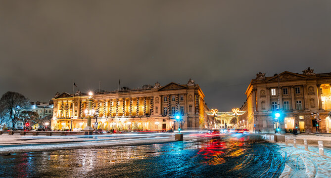 Historic buildings illuminated at night around Place de la Concorde covered in snow during winter season in Paris, France.