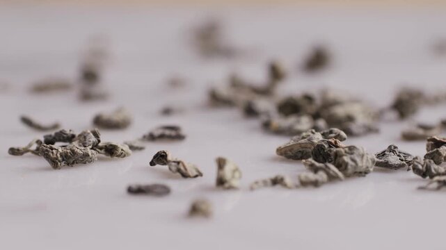 Green dried gunpowder chinese tea leaves with scoop on white wooden background, closeup.