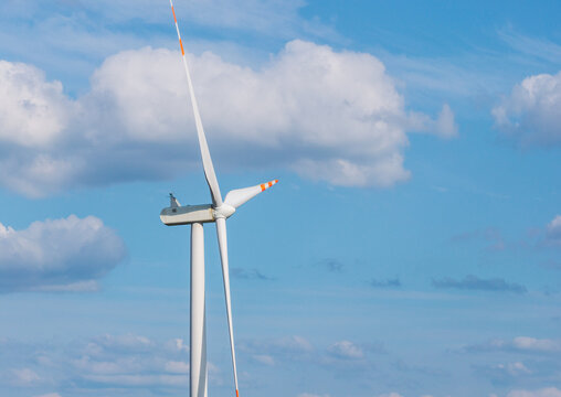 Aerial view of a white wind turbine with orange-tipped blades against a blue sky with scattered white clouds in Lebork, Pomeranian Voivodeship, Poland.