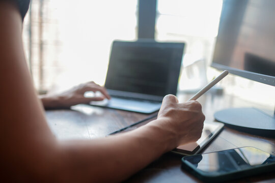 Creative professional focusing on design work from a home office. Skillfully managing multiple digital screens including a tablet with a stylus. A laptop