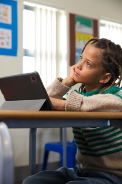African American boy child sitting at school desk wearing striped sweater and using tablet in folio