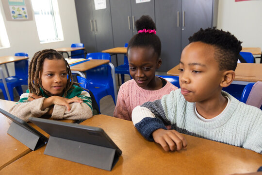 African American school children leaning over tablets on wooden classroom table using folio stands