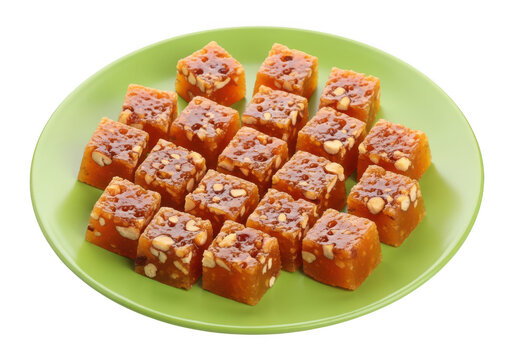A large plate of delicious indian sweet bright orange yummy kozhikode halwa cubes with nuts served on a light green plate isolated on transparent background