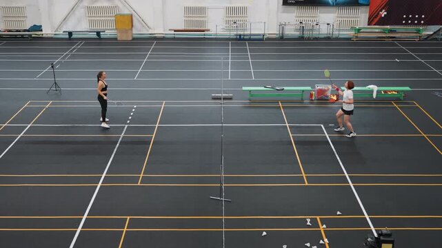 Indoor badminton court lively rally between two players exchanging fast smashes and returns. Airborne shuttlecock, rapid footwork and agile lunges, visible net and court lines, dynamic energy, amateur