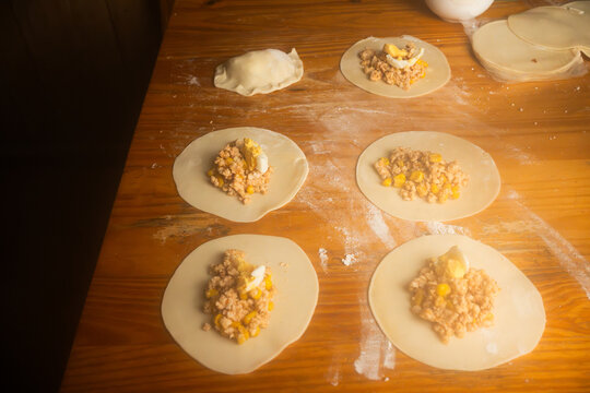 High angle view of homemade empanadas being prepared with minced meat and egg on a wooden table, Top view of raw empanada dough circles with meat filling ready for folding