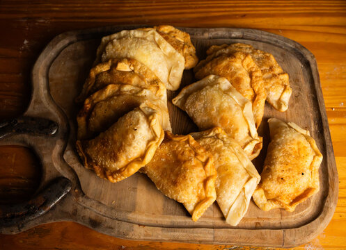 Top view of freshly baked golden brown empanadas on a rustic wooden board