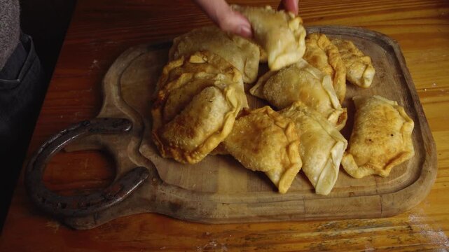 High Angle Shot of Hand Splitting Fried Empanada on Wooden Board