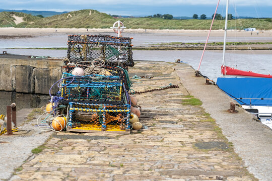 Crab pots, lobster pots and fish traps stacked on the quay in Beadnell Bay harbour, showing a traditional working fishing harbour on the Northumberland coast.