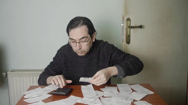 Caucasian Man Managing Home Finance and Accounting with Calculator and Invoices