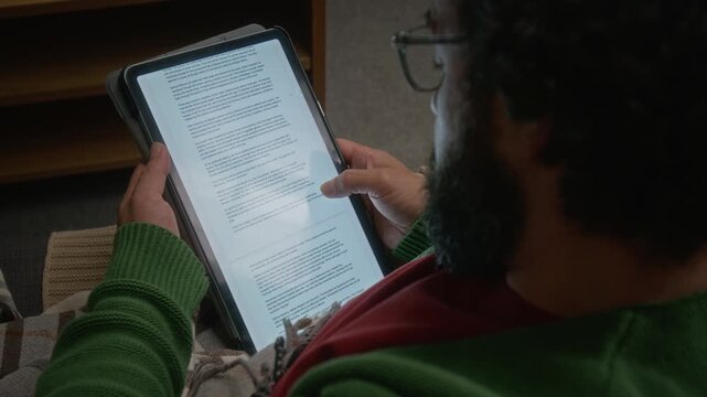 Bearded man reading e-book on tablet computer, scrolling through pages. Clip is perfect for promoting digital publishing, e-reader apps, and online education platforms