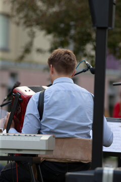 Caucasian teenage accordionist playing red instrument onstage, student soloist vibe with focused hands on buttons, festival audience blurred, youthful