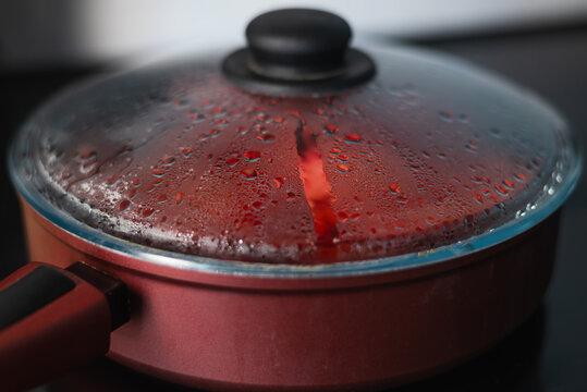 A pot sits on a stove, covered with a lid that is fogged up with steam.