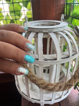 Mano mostrando manicura decorada con motivos veraniegos sobre un farol de madera blanco