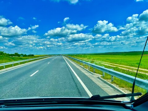 Carretera cruzando campos verdes bajo un cielo azul nublado