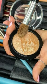 Makeup brush picks shimmering bronzer from a cosmetic compact in close up, professional beauty tools, makeup preparation, color selection.