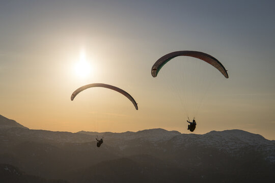 Aerial view of paragliders soaring over the Dachstein mountains during golden hour with snow-capped peaks in the background in Grobming, Styria, Austria.