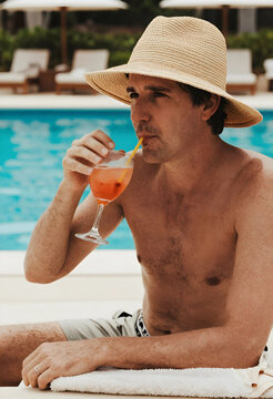Man in straw hat drinking a refreshing cocktail by the swimming pool on a sunny vacation day
