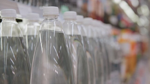 Closeup rows of clear water bottles on shelf, glistening caps and reflective surfaces, shopper hand reaching for chilled bottle, bright supermarket lighting and blurred colorful aisle background,