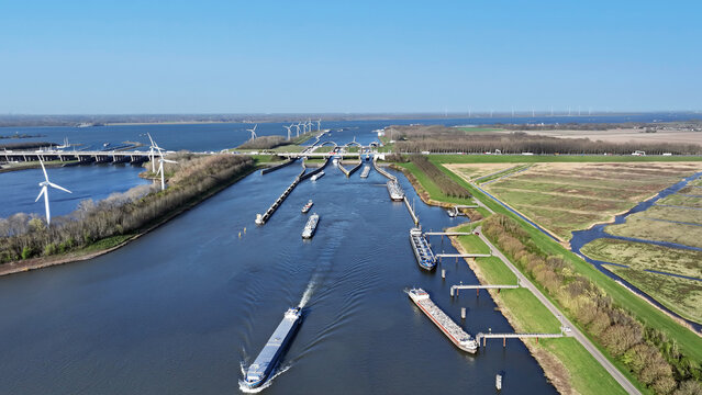 Aerial view of the Volkerak locks with cargo ships navigating the waterway, surrounded by wind turbines and green landscape in Willemstad, Noord-Brabant, Netherlands.