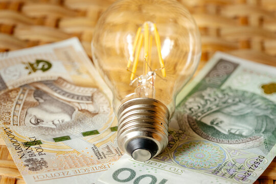 Electricity cost increase concept in Poland with light bulb on Polish Zloty banknotes background. Energy crisis, household utility bills and inflation economy.
