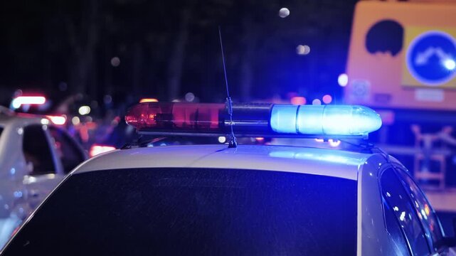 Police car roof with flashing red and blue emergency lights at night in an urban setting
