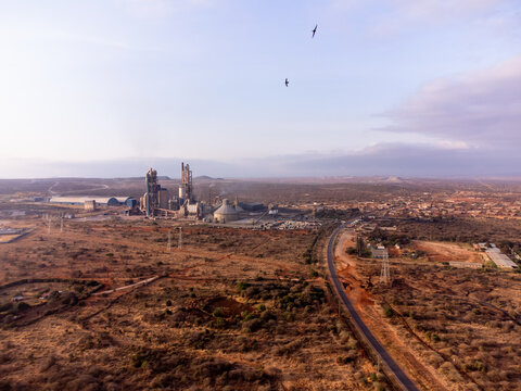 Aerial view of Simba Cement Merueshi factory set in an arid landscape with industrial structures, a nearby road, and birds flying in the sky in Kajiado, Kajiado County, Kenya.