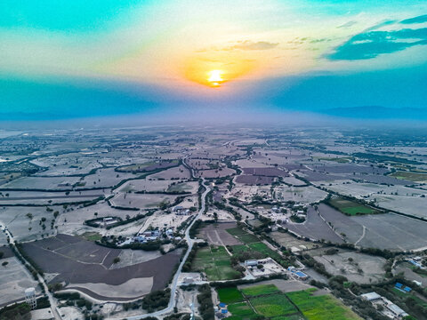 Aerial view of the Wadoor landscape during sunset, featuring agricultural fields, winding roads, and scattered settlements under a glowing sky in Dera Ghazi Khan, Punjab, Pakistan.