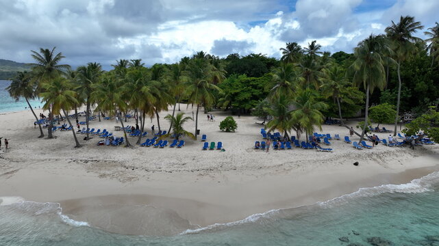 Aerial view of Cayo Levantado beach with rows of blue lounge chairs under palm trees and turquoise water in Samana, Dominican Republic.