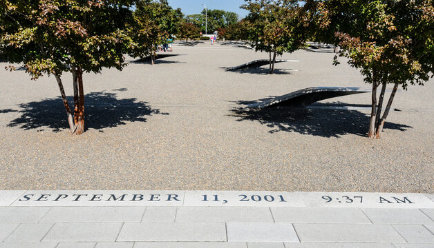 Quiet Memorial Plaza in front of the Pentagon in Washington, D.C. featuring engraved date 'September 11, 2001 9:37 AM', curved reflective benches, and small trees conveying remembrance and solemnity. 