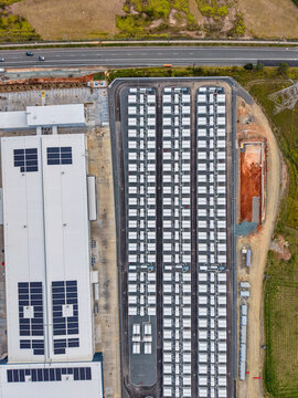 Aerial view of the Brendale BESS facility with rows of battery storage units and a large industrial building with solar panels on the roof in Brendale, Queensland, Australia.