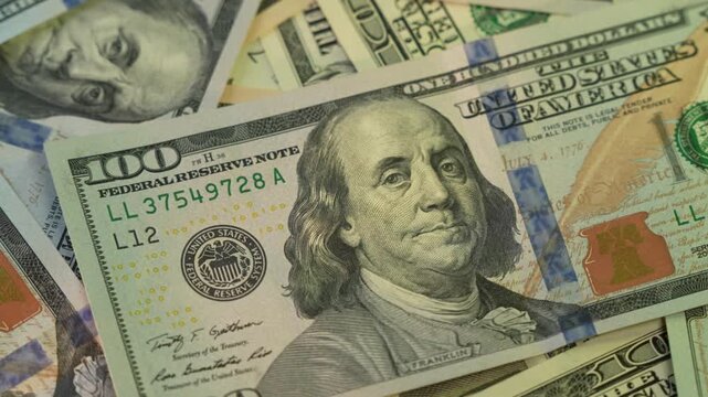 Hundred dollar bills lay scattered across a flat surface providing a detailed close up of the currency.