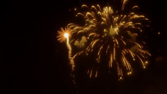 Slow motion static shot of golden fireworks exploding and cascading in night sky during outdoor celebration and festival display