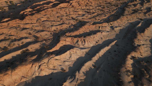 Aerial view of the rugged Valles Calchaquies landscape featuring arid rock formations, deep shadows, and sparse desert vegetation in San Carlos, Salta, Argentina.