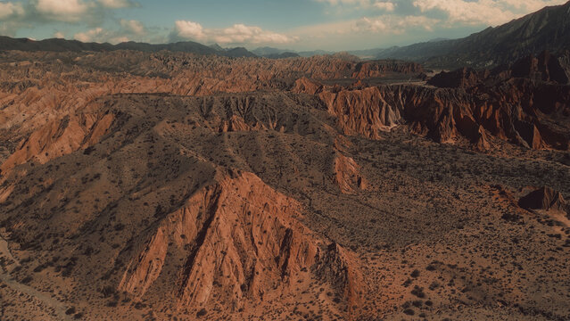 Aerial view of Valles Calchaquies featuring rugged red rock formations, arid desert landscape, and dramatic mountain ridges in San Carlos, Salta, Argentina.