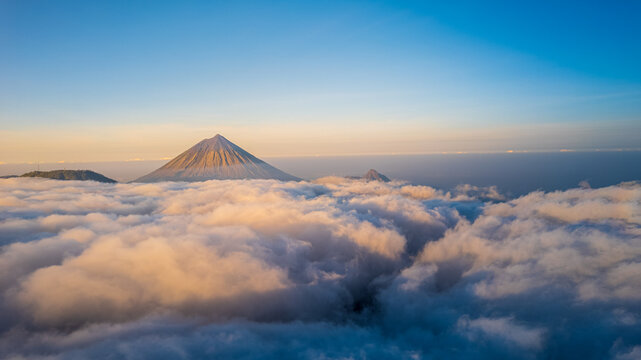 Aerial view of Mount Inerie rising above a thick sea of clouds during golden hour in Inerie, East Nusa Tenggara, Indonesia.