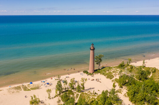 Aerial view of Little Sable Point Lighthouse standing on the sandy shore of Lake Michigan with people on the beach and green trees in Mears, Michigan, United States.