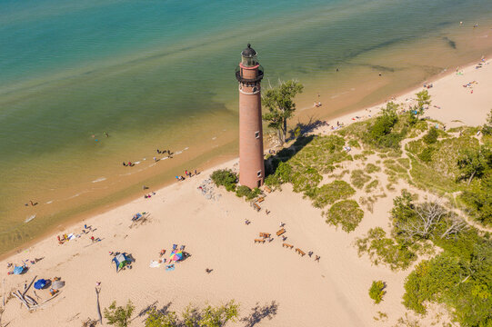 Aerial view of Little Sable Point Lighthouse standing on a sandy beach along the shore of Lake Michigan with people relaxing on the sand in Mears, Michigan, United States.