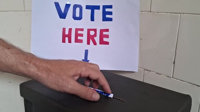 Person inserting paper ballot into dark box