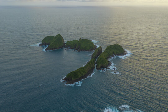 Aerial view of Green Island Banyuwangi featuring lush green vegetation on rocky islets surrounded by deep blue ocean waters in Kecamatan Pesanggaran, Java, Indonesia.
