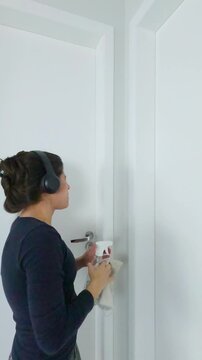 Young woman having a joyful cleaning routine wearing headphones dancing and singing while wiping the doors