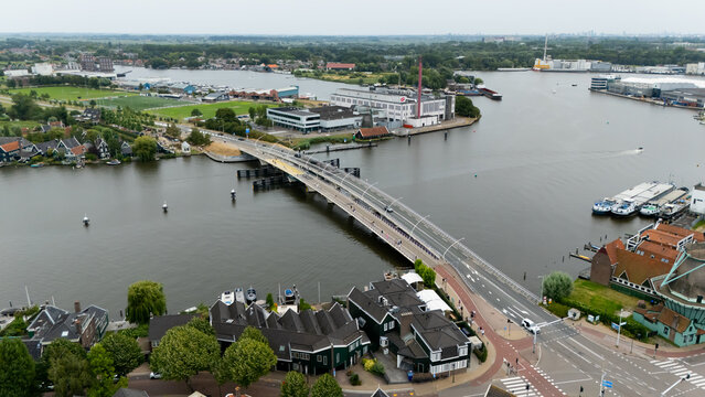 Aerial view of a bridge crossing the Zaan river, surrounded by traditional Dutch houses, industrial buildings, and boats in Zaandam, North Holland, Netherlands.
