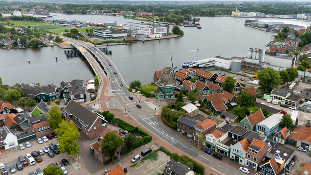 Aerial view of the Zaan river area featuring a modern bridge, a traditional Dutch windmill, and surrounding residential and industrial buildings in Zaandam, North Holland, Netherlands.