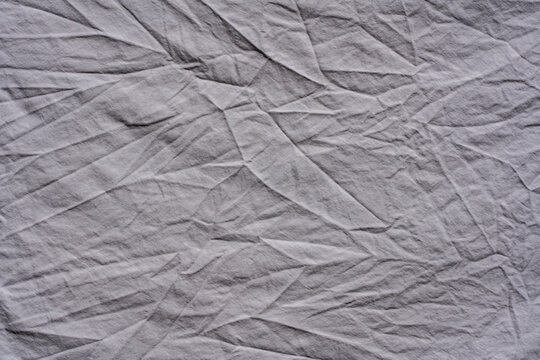 Full frame macro background of crumpled grey textile. Top view close up shot of heavily crumpled and wrinkled white fabric with complex pattern of sharp folds and deep creases