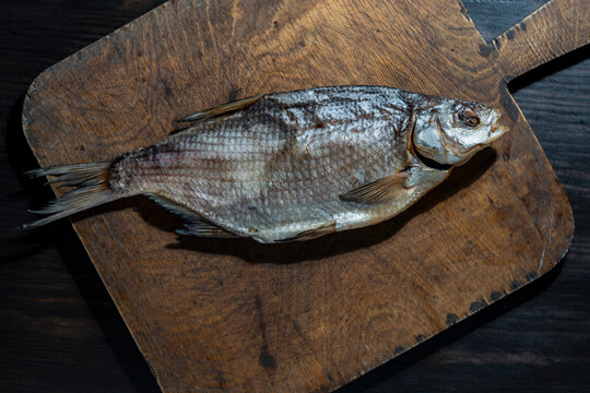 Traditional dried salted fish on rustic wooden cutting board. Top view closeup of whole salted dried bream or roach fish resting on an old textured wooden cutting board over dark background