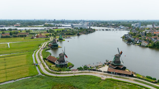 Aerial view of the historic Zaanse Schans windmills along the river with lush green fields, walking paths, and traditional Dutch architecture in Zaandam, North Holland, Netherlands.