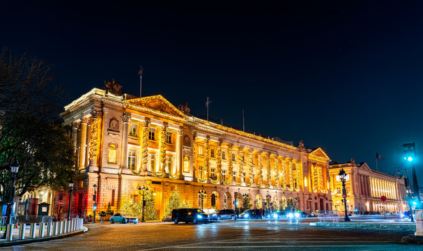 Historic neoclassical palace decorated with festive golden Christmas lights at night on Place de la Concorde in Paris, France.