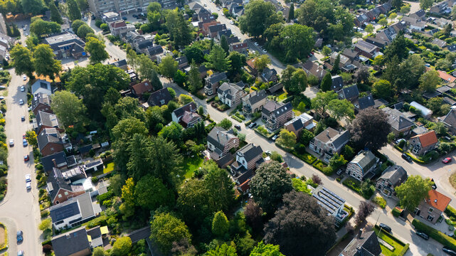 Aerial view of a residential neighborhood with detached houses, lush green trees, well-maintained gardens, and winding streets in Apeldoorn, Gelderland, Netherlands.