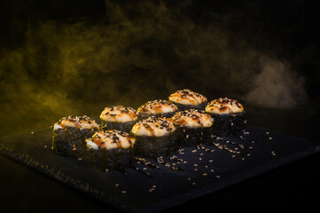 Hot Baked Sushi Rolls with Light Smoke on Black Background © Ilias