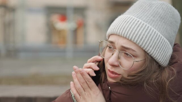 Caucasian woman friend urgent phone call on park bench, animated expression and pleading gesture, winter jacket and knit hat, close conversational framing with raw emotion and human connection