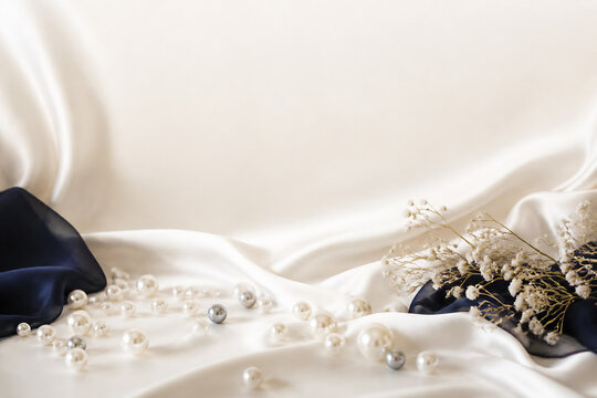 Pearls and delicate white flowers are scattered across draped white satin fabric.